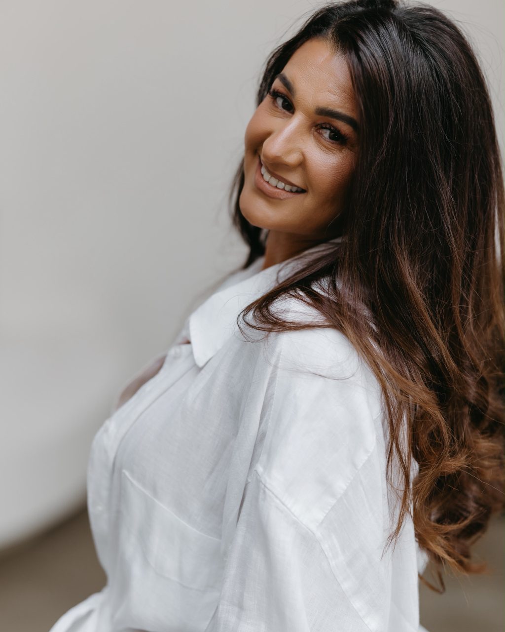 Fatima staat in een witte linnen blouse en kijkt glimlachend over haar schouder naar de camera